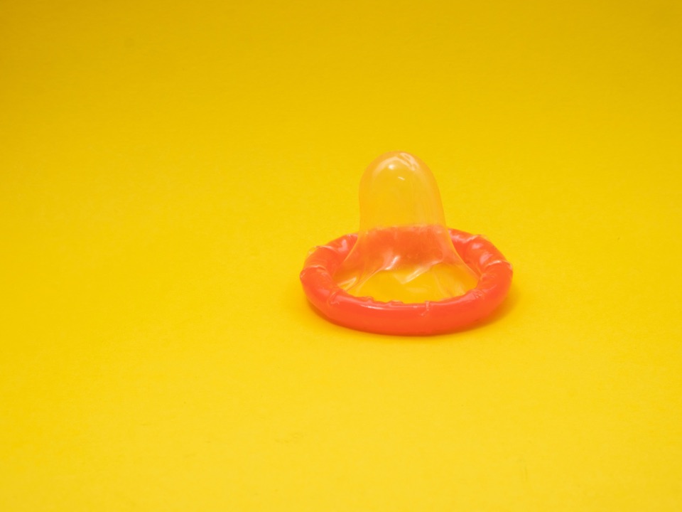 Bild eines ausgepackten, orangefarbenen Kondoms auf gelbem Hintergrund.