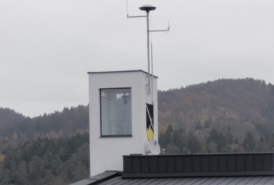 Auf dem Dach eines Feuerwehrhauses ist eine deutlich sichtbare Sirene angebracht.