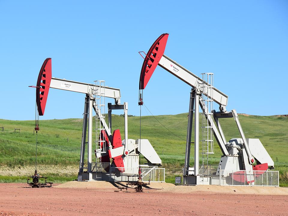 Zwei rot-weiße Erdölförderpumpen auf einem Feld vor einer grünen Wiese
