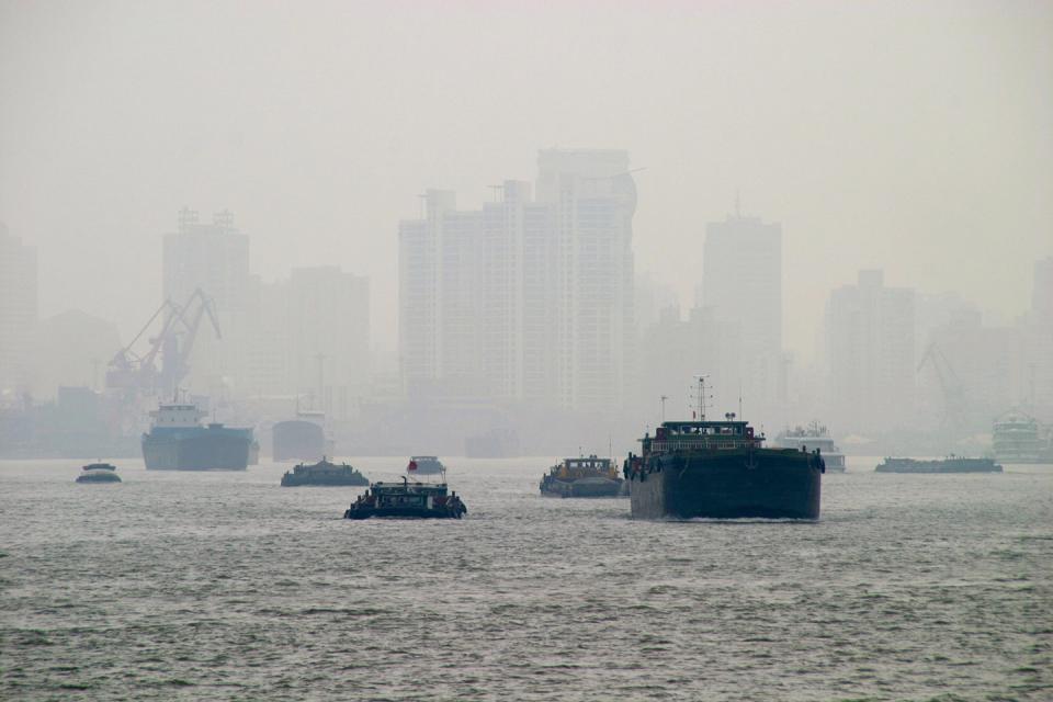 Smog über dem Meer und einer Großstadt. Die Schiffe sind durch den Nebel kaum noch sichtbar.