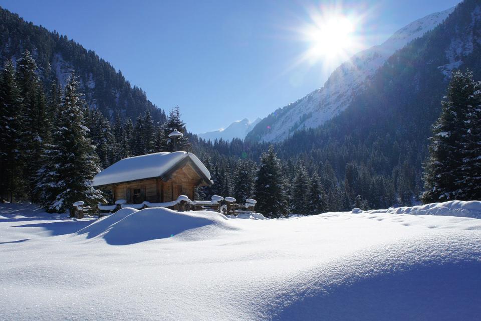 Eine verschneite Hütte in einem Tal bei Sonnenschein