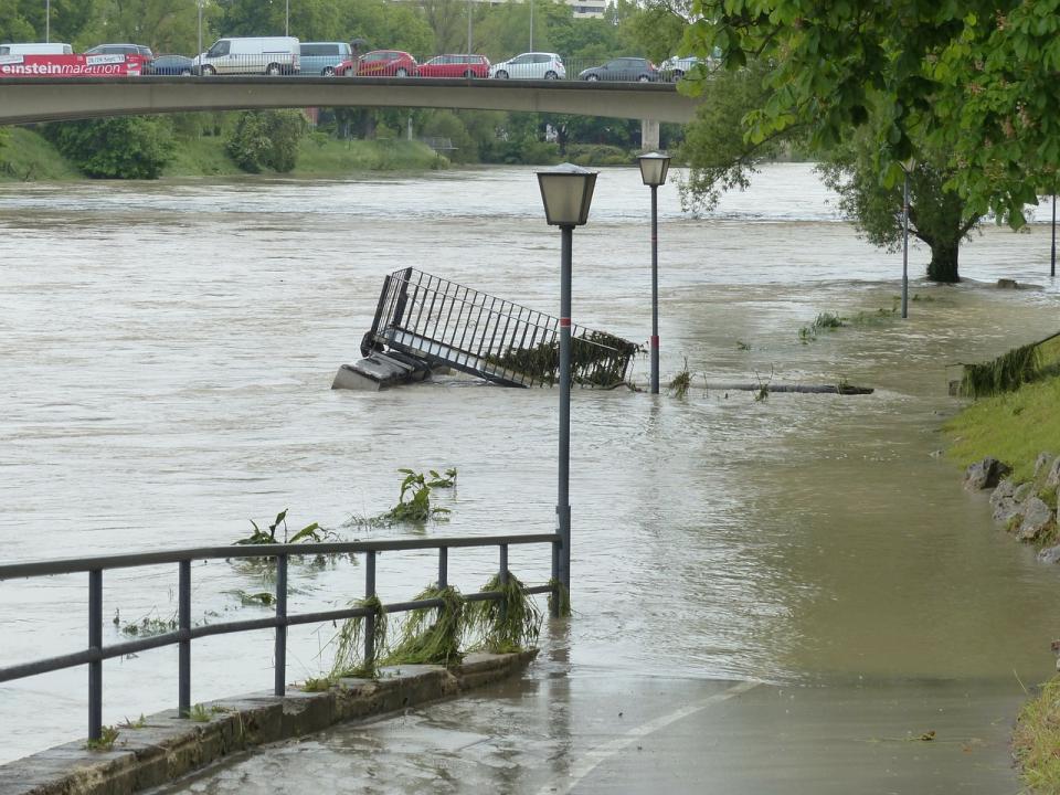 Ein Bild einses überschwemmten Radweges, welche noch durch Straßenlaternen zuordenbar ist, im Hintergrund ein Autostau auf der Brücke.