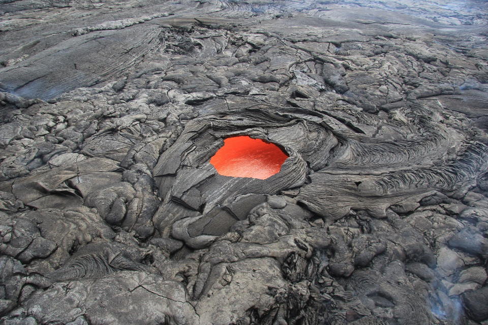 Bild einer erstarrten Lavalandschaft, dessen Kruste in der Mitte rund aufgebrochen ist und rote flüssige Lava durchscheint.
