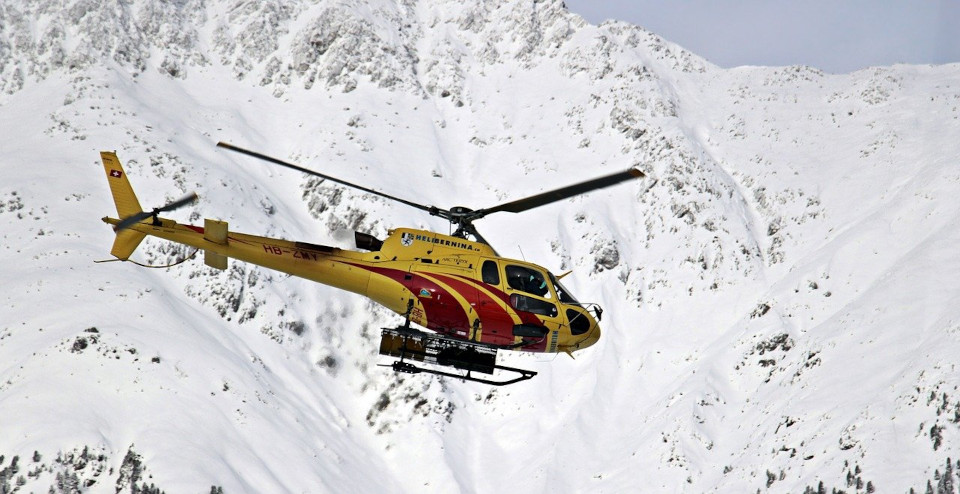 Ein gelber Rettungshubschrauber fliegt über einen schneebedeckten Berg