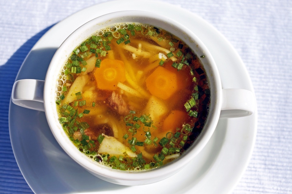 Suppe in einer Tasse. In der Suppe sind Nudeln, Karotten und Rindfleischstücke
