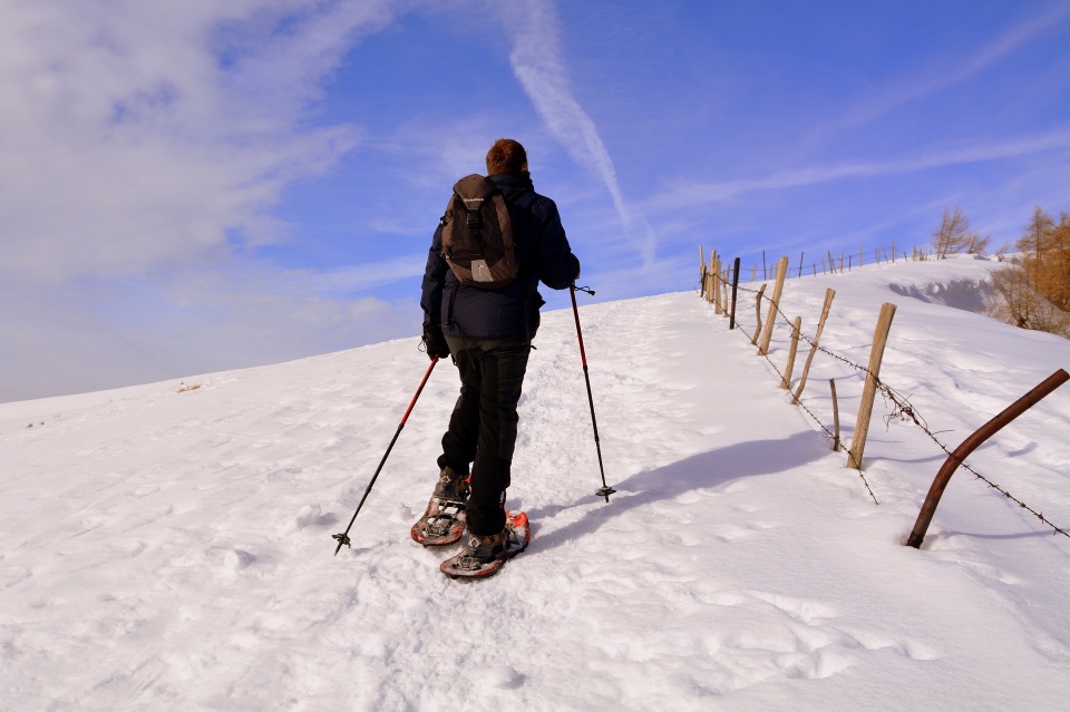 Ein Wanderer mit Schneeschuhen geht einen verschneiten Berg hinauf