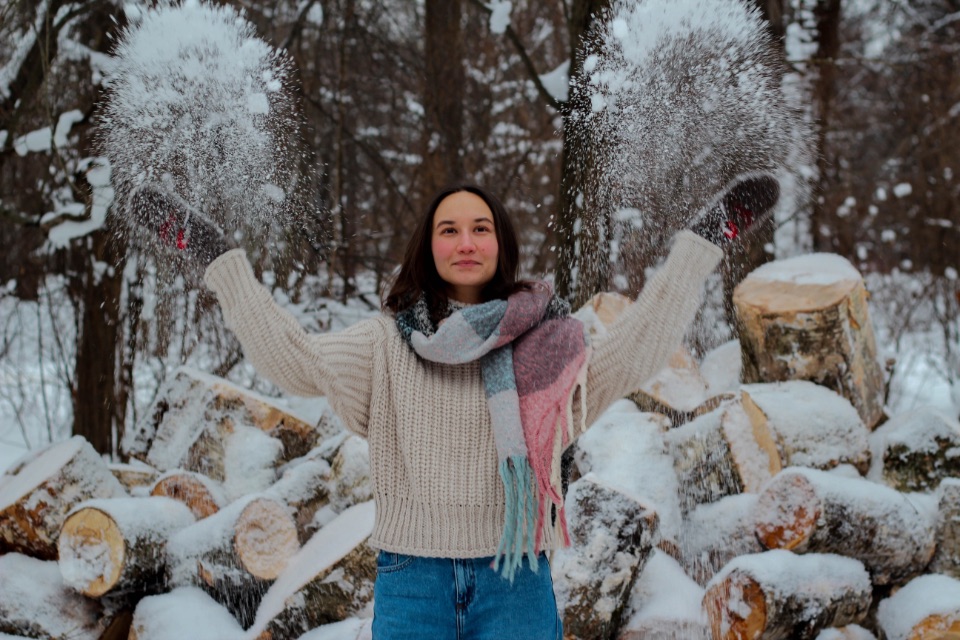 Eine Frau hat einen Pullover und Handschuhe an und schmeißt Schnee in die Luft.